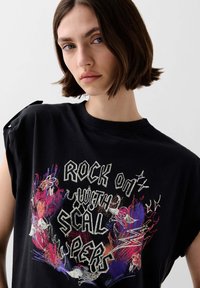 Black cotton t-shirt featuring a colorful graphic design with the text "ROCK ON WITH SCALPERS," short sleeves with tied accents.