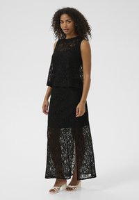 Robe noire en dentelle en deux pièces avec un haut sans manches à col haut et une longue jupe transparente avec une fente sur le côté.