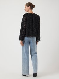 Schwarzer strukturierter Pullover mit langen Ärmeln, der ein fransiges Design und eine lockere Passform aufweist, kombiniert mit hoch taillierten hellblauen Jeans.