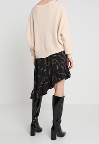 Vaaleanpunainen, löysä neulepusero, jossa on pudotetut olkapäät, yhdistettynä mustaan, epäsymmetriseen hameeseen, jossa on kultaisia ja sinisiä kuvioita. Polven yli ulottuvat kiiltävät mustat saappaat.