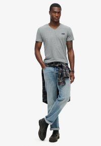 Grå v-hals t-shirt, lyseblå jeans, sort ternet skjorte bundet om taljen, sorte ankelstøvler med tekstureret finish. Uformelt tøj vist.