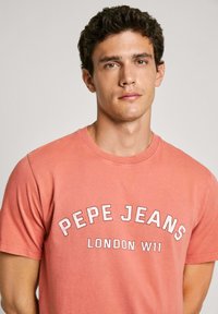 Ružový bavlnený tričko s potlačou "PEPE JEANS" a "LONDON W11" v bielej farbe, krátke rukávy, okrúhly výstrih a voľný strih.