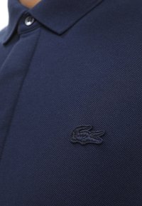 Navy blue polo shirt made of textured fabric, featuring a button-down collar and a small embroidered logo on the left chest.