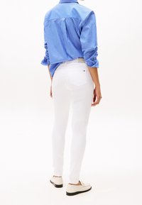 Bílé úzké džínsy s hladkou texturou, spárované s modro-bílou pruhovanou košilí na knoflíky. Bílé volnočasové boty dokončují outfit.