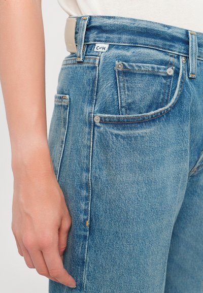 Jeans in denim blu chiaro con un design a vita alta, dotati di passanti per la cintura, cinque tasche e dettagli in metallo. Texture liscia e vestibilità classica.