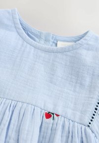 Helles blaues Baumwollkleid mit bestickten roten Kirschen, gefälteltem Oberteil und rundem Halsausschnitt mit einer kleinen Knopfdetaillierung auf der Rückseite.