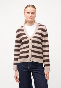 Καρό πλεκτό ζακέτα σε μπεζ και καφέ, κατασκευασμένη από μαλακό υλικό. Διαθέτει V-λαιμόκοψη, πέντε κουμπιά και μπροστινές τσέπες.