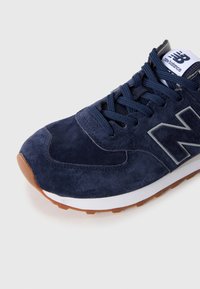 Baskets New Balance en daim bleu marine avec des lacets bleu foncé, une semelle blanche et marron, et un grand logo "N" sur le côté.