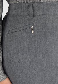 Jupe crayon grise en tissu texturé, avec une poche zippée, une ceinture et des détails de couture latérale.