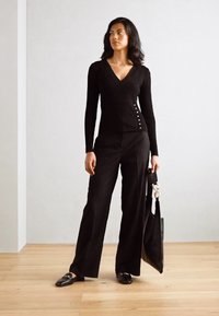 Pull noir côtelé avec un col en V, doté de boutons sur le côté. Associe avec un pantalon large noir taille haute et un sac fourre-tout noir.