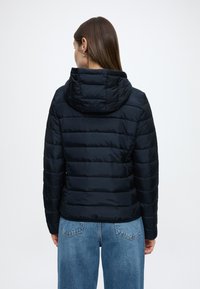 Μπουφάν puffer σε ναυτικό μπλε με κουκούλα, με ραμμένες επενδύσεις και λεία υφή, συνδυασμένο με ανοιχτό μπλε παντελόνι με φαρδιά πόδια.