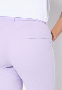 Lila broek van stretchy stof, met een gladde textuur, een achterzakdetail en een strakke pasvorm. De tailleband is subtiel.