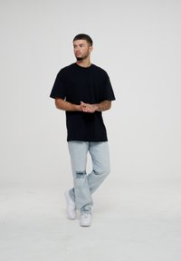 Svart bomull t-skjorte med en avslappet passform, kombinert med lyseblå slitte jeans med en synlig rivning. Hvite sneakers fullfører antrekket.