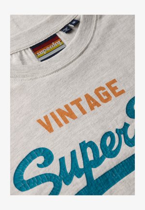 T-shirt in cotone grigio chiaro con la scritta "VINTAGE" in arancione e "Superdry" in lettere testurizzate color teal, con design a collo rotondo.