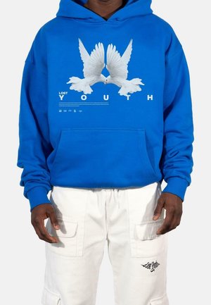 Felpa blu con grafica bianca di due colombe, il testo "LOST YOUTH" sotto. Presenta tasca a marsupio e polsini a coste. Pantaloni cargo bianchi.