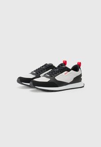Sorte og hvite sneakers med en glatt tekstiloverdel, polstret krage, rød aksent ved hælen og en teksturert gummisåle.