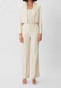 Beige kort blazer och matchande högmidjade vida byxor, tillverkade av mjukt tyg, kompletterat med ett bälte och en ribbad linneblus under.