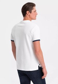 Polo bianca con maniche corte, dettagli blu navy sui polsini e sul colletto, tessuto strutturato, orlo dritto e spacco laterale.