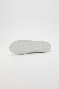 Podplat bele športne superge z rahlo teksturiranim vzorcem za oprijem in vrezanim logotipom "ck" na sredini, prikazan na enobarvnem belem ozadju.