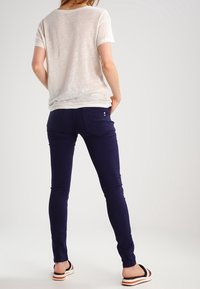 White, loose-fitting t-shirt with a round neckline; paired with form-fitting, dark purple jeans; flat sandals with black and orange stripes.