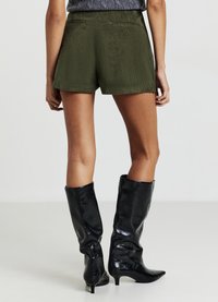 Pantaloncini verdi in velluto a coste con taglio dritto, dotati di due tasche posteriori. Abbinati a stivali neri in vernice al ginocchio.