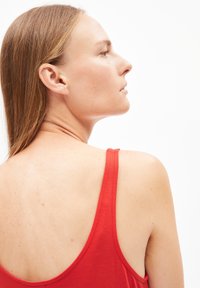 Rode tanktop met dunne bandjes, zachte stof en een brede armsgatontwerp, waarbij huid op de rug en schouder zichtbaar is.