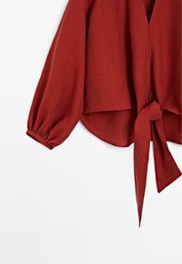 Rød, let bluse med lange pufærmer og en knudemærke ved taljen. Stoffet har et struktureret, vævet udseende.