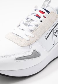 Białe sneakersy z miękką zamszową nakładką i szarymi akcentami. Oferują teksturowaną wstawkę, białe sznurowadła i logo na boku.