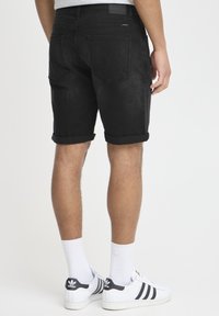 Shorts en denim noirs avec des revers, dotés de poches arrière et d'un écusson en cuir de marque. Portés avec des baskets blanches et des chaussettes.
