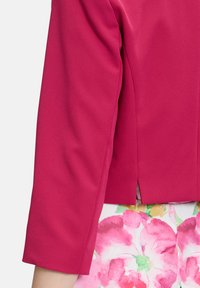 Fitted, cropped jasje van helderroze stof met een gladde textuur en driekwart mouwen, gecombineerd met een rok met bloemenpatroon.