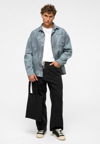 Lichtblauw knoopshirt, witte t-shirt, zwarte jeans, zwarte tote tas en zwarte sneakers. Eenvoudig ontwerp, ontspannen pasvorm, gestructureerde stof.