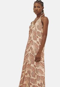 Vestido maxi en beige claro con un estampado de abanicos rojos. Presenta un diseño de cuello halter, tela fluida y bolsillos laterales para mayor comodidad.