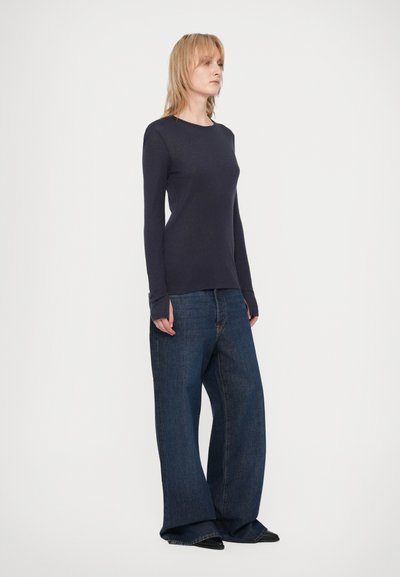 Tricou de culoare bleumarin cu mânecă lungă și guler rotund, asociat cu blugi întunecați cu croială largă. Material neted, croială lejeră și detalii de cusătură subtile.