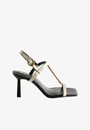 Högklackad sandal med kvadratisk tå, svart lädersula, beige remmar, detaljer i guldkedja och justerbar ankelspänne.