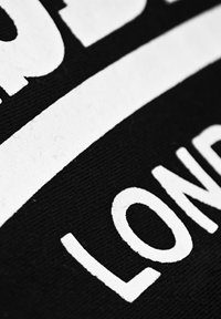 Črna tkanina z bold belim besedilom, ki pravi "LONDON." Očitna tekstura tkanine in gladke, kontrastne črke.
