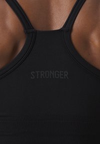 Mustaga spordibrasi, millel on sile kangas, tihe istuvus ja tekstuuriga elastne riba, millele on prinditud vaikses tumedas värvitoonis "STRONGER" logo.