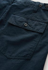 Navy blue-farbige Stoffshorts mit einer geknöpften Klappentasche, glatter Textur und kontrastierenden Nähten an den Rändern. Zwei Knöpfe an der Taille.