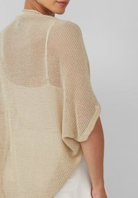 Beige open-knit cardigan met een losse pasvorm, met korte mouwen en een zachte, getextureerde uitstraling. Achterkant toont het gaaspatroon.