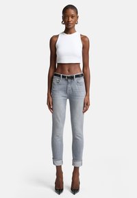 Lichtgrijze skinny jeans met opgerolde cuffs, gecombineerd met een witte geribbelde cropped tanktop. Zwarte riem met zilveren hardwareaccenten.