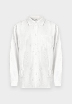 Chemise blanche à manches longues avec un col à boutons, présentant des embellissements texturés et une poche poitrine, fabriquée dans un tissu léger.