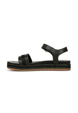 Black sandals featuring woven texture straps, a flat sole with a slight lift, and a rubber outsole with a ridged pattern for grip.