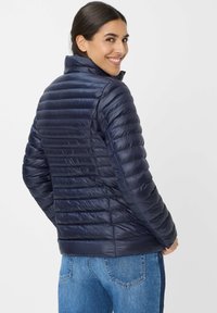 Marineblauer Daunenjacke mit gestepptem Design, hohem Kragen und glänzender Textur, kombiniert mit blauen Jeans. Ansicht von hinten.