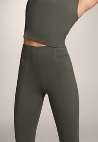 Top sportivo corto color verde oliva e leggings a vita alta. Tessuto morbido ed elastico con dettagli di cuciture verticali e accenti laterali sui leggings.