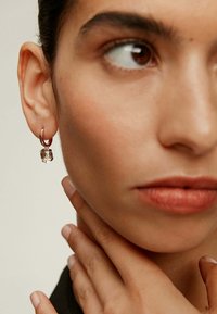 Pendiente de aro de plata con un detalle de gema transparente, llevado en la oreja izquierda de una persona. Textura suave y diseño minimalista destacado.