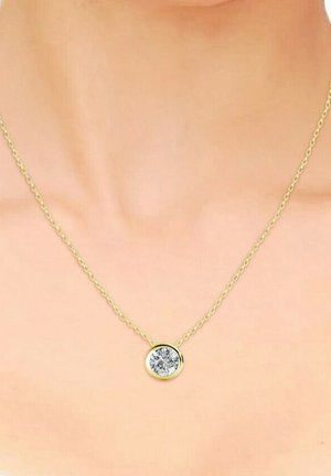 Collana in oro con pendente a forma di pietra rotonda e trasparente, finitura lucida e delicati collegamenti, poggiata su uno sfondo di tonalità della pelle neutra.