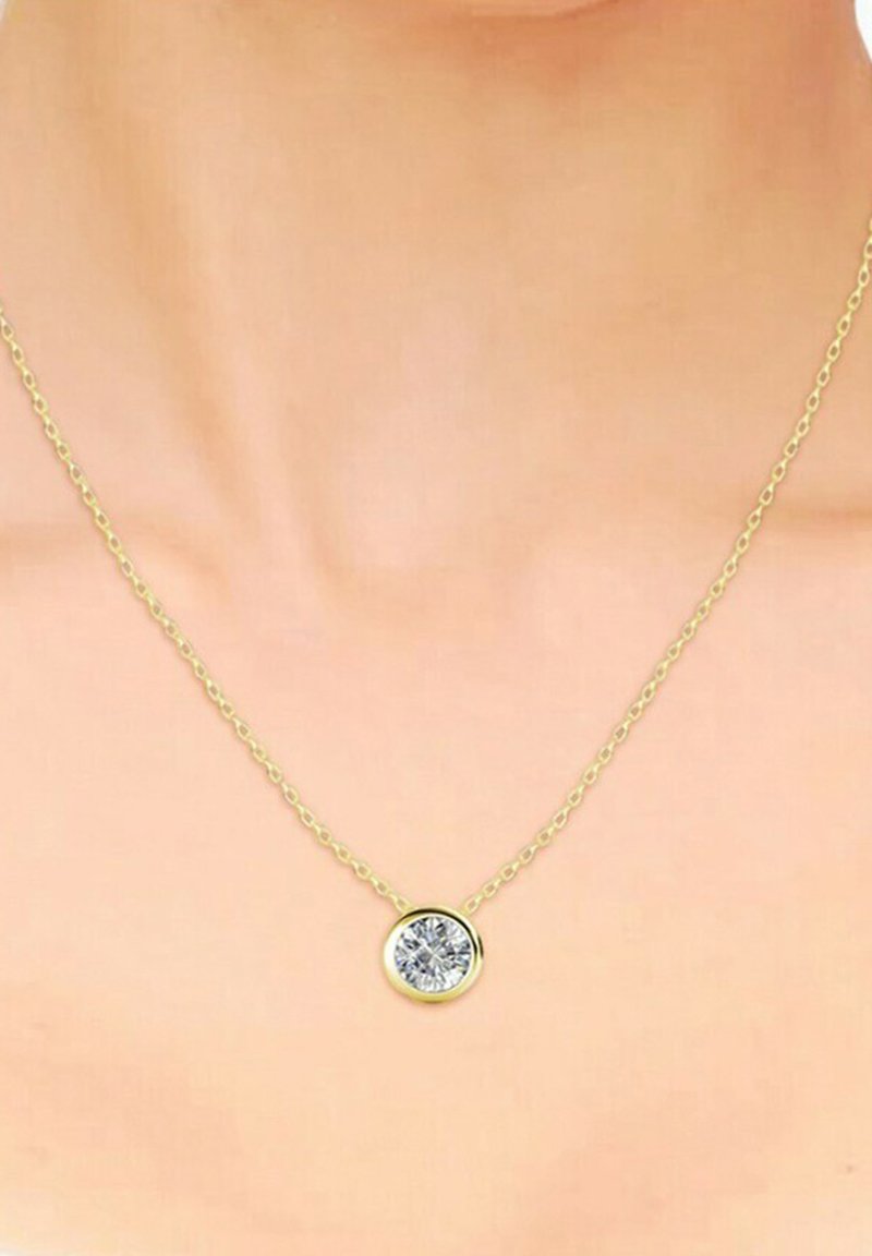 Collier en chaîne dorée avec un pendentif rond en pierre claire, finition polie et maillons délicats, reposant sur un fond de teint neutre.