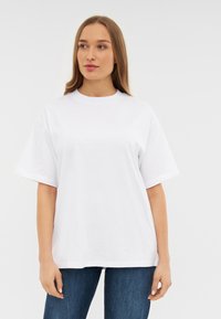 Camiseta de algodón blanca con mangas cortas, cuello redondo y corte relajado. El material parece suave y liso, con un diseño mínimo o sin logotipos.