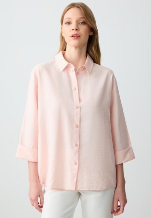 Camicia rosa chiaro con bottoni realizzata in un tessuto strutturato, dotata di colletto, maniche a tre quarti e polsini con bottoni.