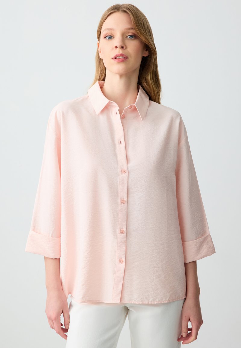 Camicia rosa chiaro con bottoni realizzata in un tessuto strutturato, dotata di colletto, maniche a tre quarti e polsini con bottoni.