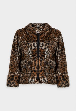 Femme portant une veste en fausse fourrure à imprimé léopard marron et noir avec une jupe assortie, un haut noir et des sandales noires à talons hauts, debout devant un fond blanc.